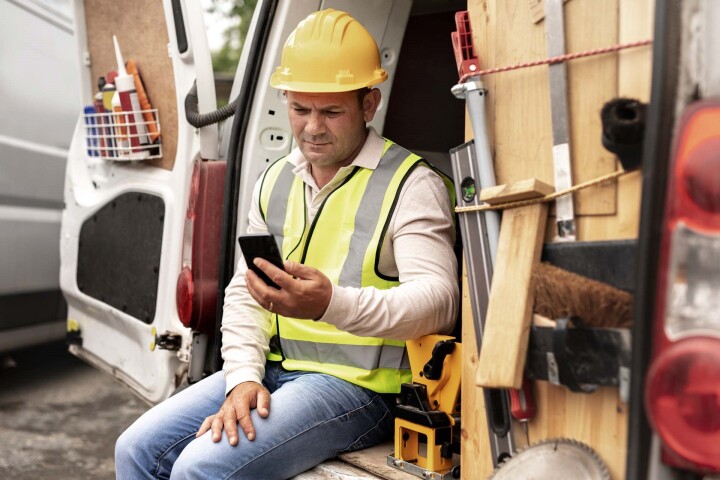 Bouwvakker in bestelwagen checkt Check-in-at-Work registratie via zijn telefoon.