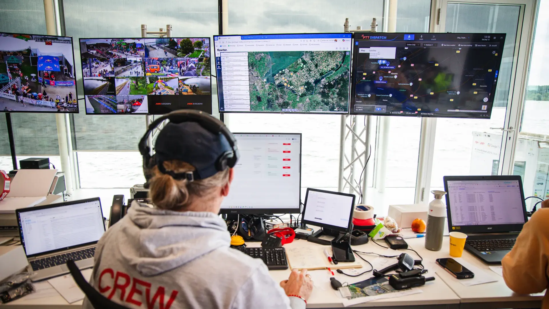 Crewmitglied mit Headset am Schreibtisch mit Laptops und Funkger&auml;ten vor Bildschirmen mit Flowter, PTT Dispatch und Kameras