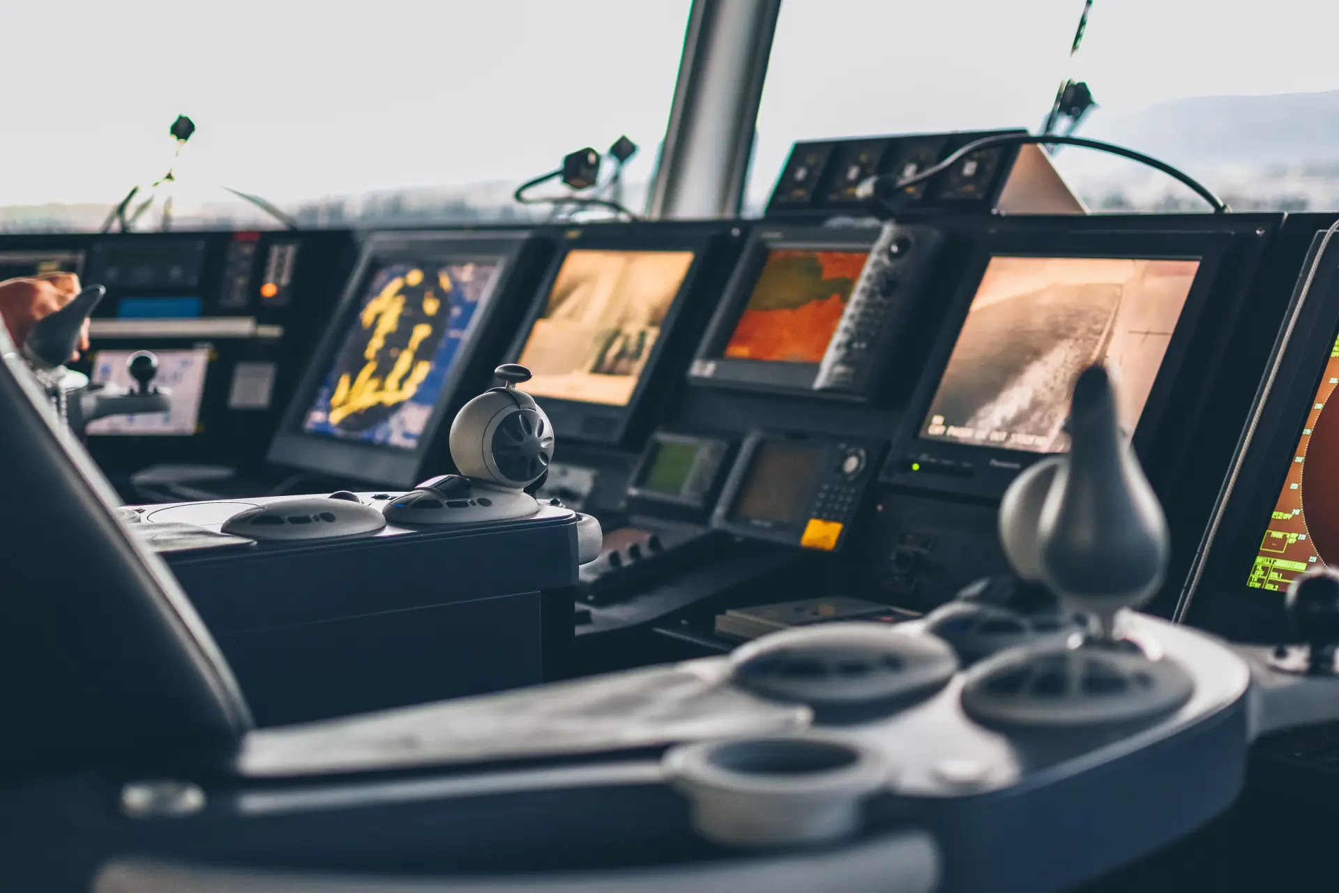 Brug van een schip met joysticks op de voorgrond en een rij navigatieschermen met radar en camerabeelden