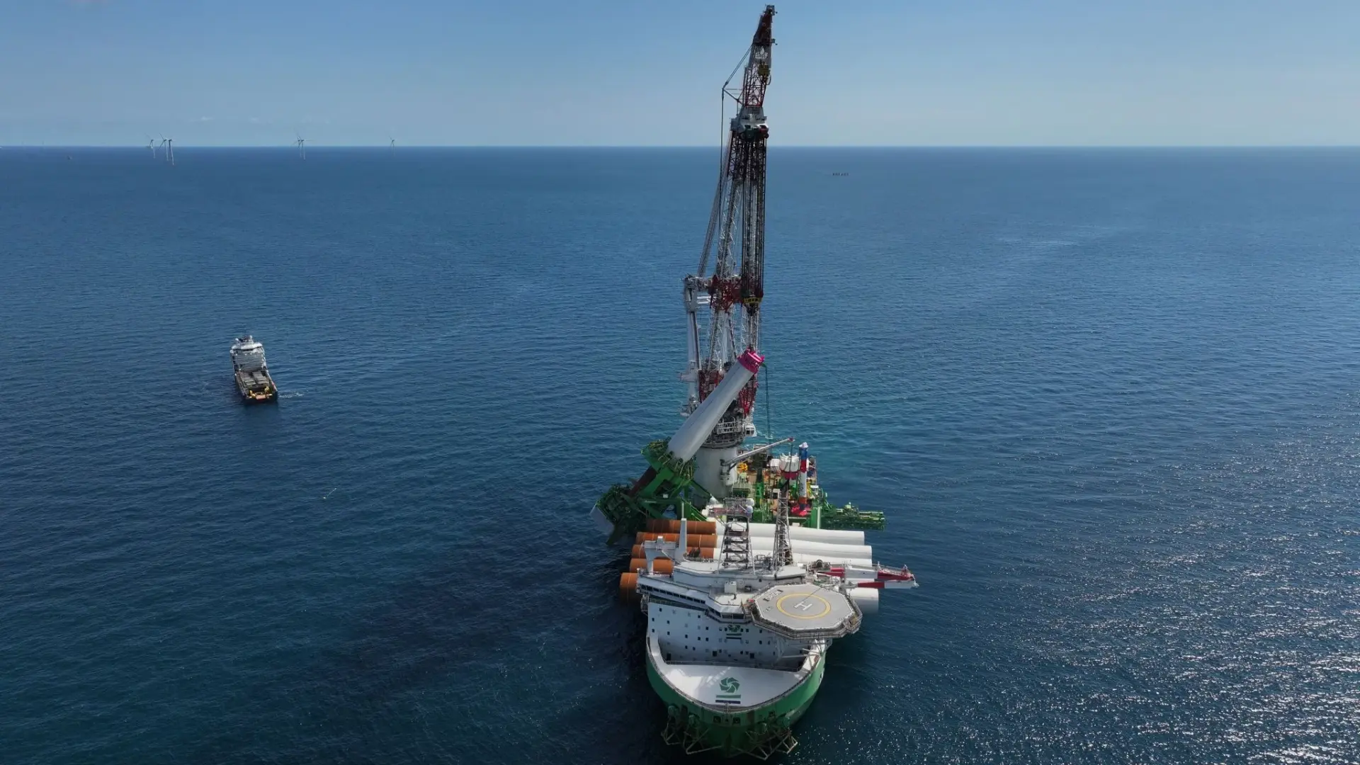 Luchtfoto van kraanschip met monopiles aan dek op zee, windturbines aan de horizon