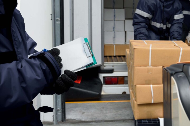 Koerier met klembord bij de laadklep van een vrachtwagen, met dozen. | GPS-Buddy