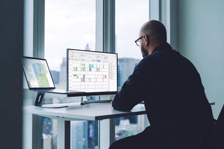 Mann vor Bildschirmen mit Fahrzeugortungssystem und Routenplanungssoftware in einem B&uuml;ro.