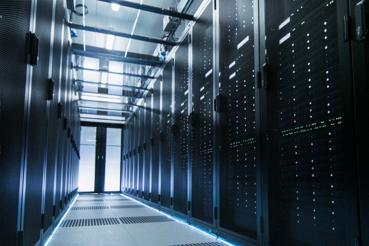 Server room aisle with black server racks and blue LED lighting on floor.