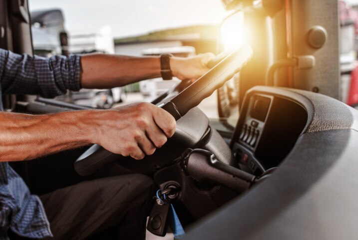 Man's hands on a truck steering wheel, sun shining, representing driving behavior insights.