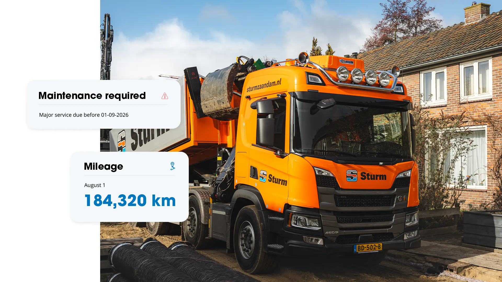 Orange Sturm tipper truck in a residential street with cards showing 184,320 km and scheduled major maintenance