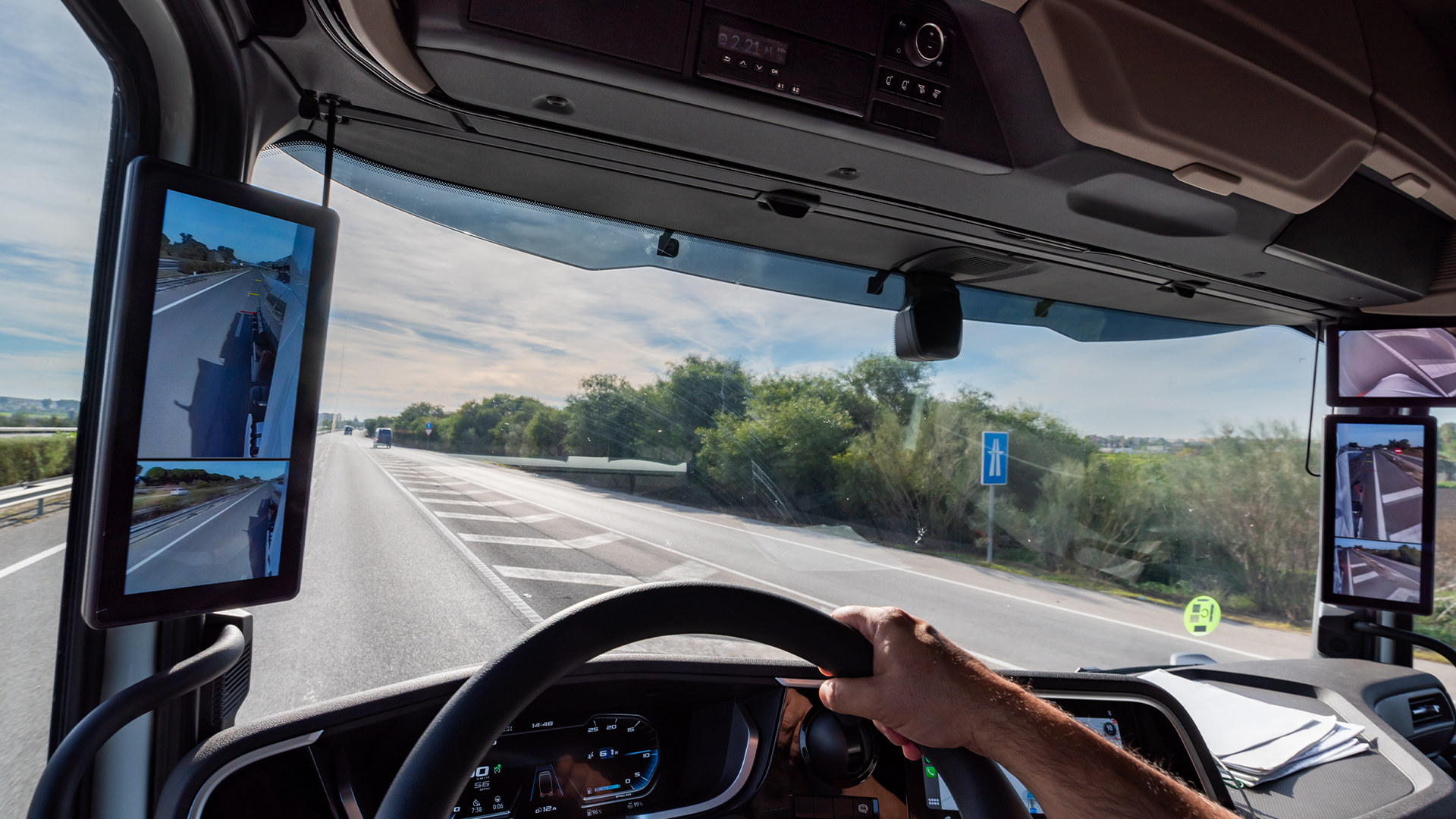 Zicht vanuit vrachtwagencabine op snelweg met digitale cameraschermen aan weerszijden van de voorruit
