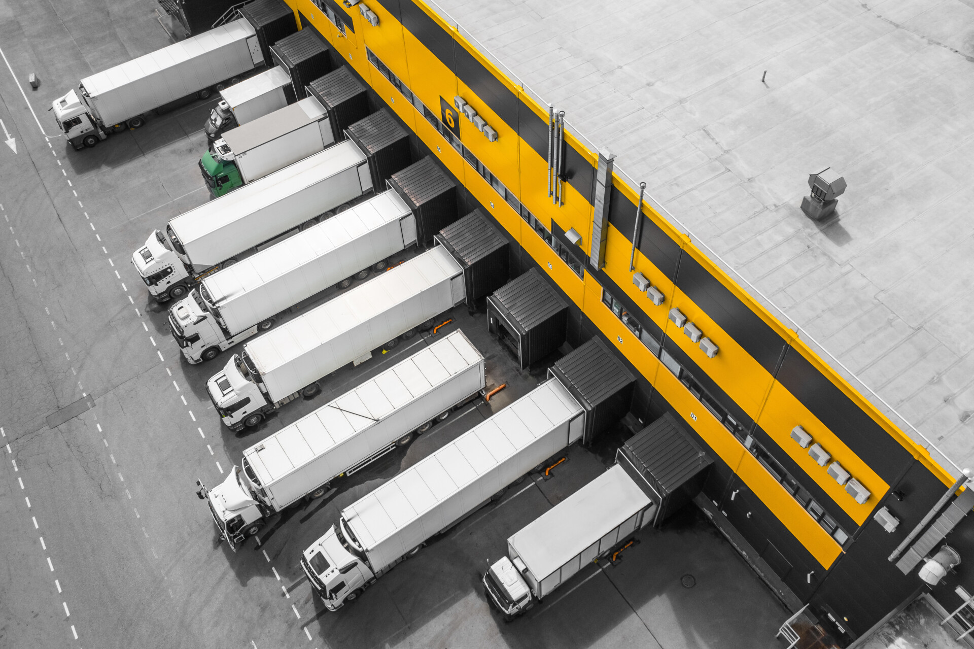 Luchtfoto van meerdere vrachtwagens met opleggers bij de laadperrons van een distributiecentrum met geel-zwarte gevel.